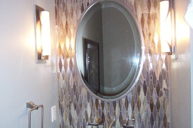 Modern inredning av ett litet toalett, med släta luckor, skåp i mörkt trä, en toalettstol med separat cisternkåpa, flerfärgad kakel, glaskakel, grå väggar, ett fristående handfat och bänkskiva i kvartsit