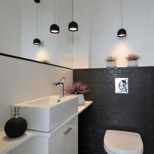 Immagine di un bagno di servizio minimal con lavabo a bacinella, ante lisce, ante bianche, WC sospeso, piastrelle nere, pareti bianche e top bianco