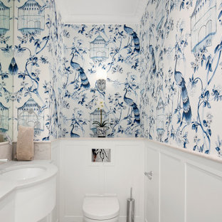 This is an example of a mid-sized beach style powder room in Sydney with white cabinets, a wall-mount toilet, marble, medium hardwood floors, an undermount sink, marble benchtops, grey benchtops, a built-in vanity and wallpaper.