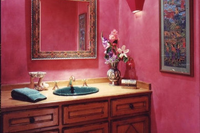 Kleine Stilmix Gästetoilette mit Einbauwaschbecken, profilierten Schrankfronten, Waschtisch aus Holz, Wandtoilette mit Spülkasten, braunem Holzboden, rosa Wandfarbe und dunklen Holzschränken in Los Angeles