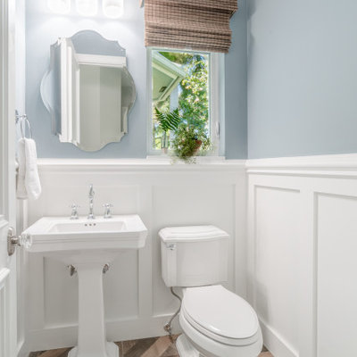 Small transitional porcelain tile, brown floor and wainscoting powder room photo in Miami with blue walls, white countertops, a two-piece toilet and a pedestal sink