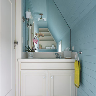 Exemple d'un petit WC et toilettes chic avec un lavabo encastré, un placard à porte affleurante, des portes de placard blanches, un plan de toilette en surface solide, un mur bleu et un sol en bois peint.