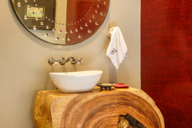 Modelo de aseo rústico de tamaño medio con lavabo sobreencimera, armarios tipo mueble, puertas de armario de madera clara, paredes rojas y encimera de madera