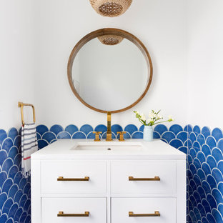 Idées déco pour un WC et toilettes bord de mer avec un placard à porte plane, des portes de placard blanches, un carrelage bleu, un mur blanc, un lavabo encastré, un sol bleu et un plan de toilette blanc.