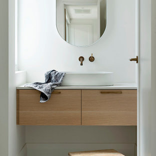 This is an example of a small contemporary powder room in Perth with medium wood cabinets, white walls, cement tiles, engineered quartz benchtops, beige floor, a floating vanity, flat-panel cabinets, a vessel sink and white benchtops.