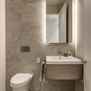 Modelo de aseo actual con sanitario de pared, armarios con paneles lisos, puertas de armario grises, baldosas y/o azulejos grises, paredes blancas, lavabo tipo consola y suelo marrón