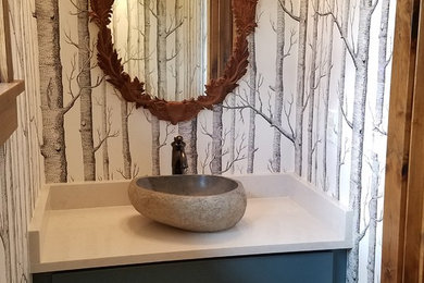 Mid-sized mountain style brown floor powder room photo in Denver with shaker cabinets, blue cabinets, multicolored walls, a vessel sink, solid surface countertops and white countertops