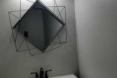 アトランタにある中くらいなトランジショナルスタイルのおしゃれなトイレ・洗面所 (落し込みパネル扉のキャビネット、黒いキャビネット、グレーの壁、一体型シンク、白い洗面カウンター) の写真
