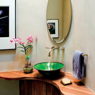 Cette image montre un WC et toilettes sud-ouest américain avec un placard à porte plane, des portes de placard en bois sombre, un mur beige, une vasque et un plan de toilette en bois.