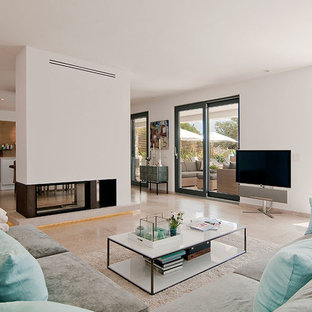 Modelo de sala de estar abierta, mediterránea, grande, con paredes blancas, suelo de piedra caliza, televisor independiente y chimenea de doble cara