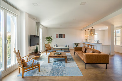 Imagen de sala de estar abierta costera grande sin chimenea con paredes blancas, suelo de madera en tonos medios y televisor colgado en la pared
