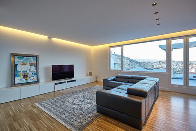 Diseño de sala de estar abierta actual grande con paredes blancas, suelo de madera en tonos medios y pared multimedia