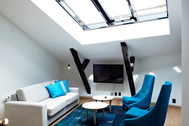 Modelo de sala de estar abierta actual de tamaño medio sin chimenea con paredes blancas, suelo de madera en tonos medios y televisor colgado en la pared