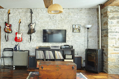 Modelo de sala de estar con rincón musical de estilo de casa de campo con paredes beige, suelo de madera en tonos medios, estufa de leña y televisor colgado en la pared