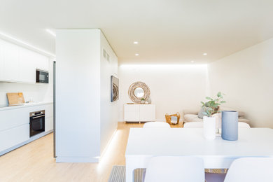 Ejemplo de sala de estar abierta actual de tamaño medio con paredes blancas, suelo de madera clara, suelo marrón y televisor colgado en la pared