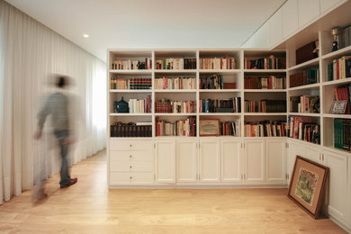 Ejemplo de sala de estar con biblioteca cerrada actual de tamaño medio sin chimenea y televisor con paredes blancas y suelo de madera clara