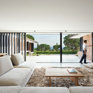 Diseño de sala de estar con biblioteca abierta, minimalista, grande, sin chimenea, con paredes beige, suelo de cemento, televisor retractable y suelo gris