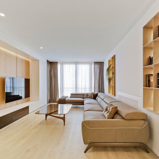Modelo de sala de estar con biblioteca contemporánea, sin chimenea, con paredes blancas, suelo de madera clara, televisor colgado en la pared y suelo beige