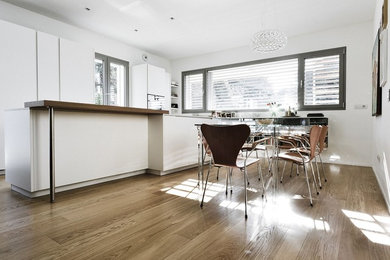 Immagine di una sala da pranzo aperta verso la cucina minimal con pareti bianche e parquet chiaro