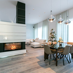 Immagine di una grande sala da pranzo design con pareti bianche, parquet scuro, camino bifacciale, cornice del camino in intonaco e pavimento grigio