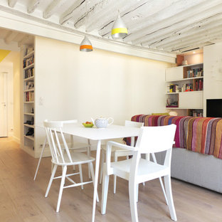 Cette image montre une salle à manger ouverte sur le salon design de taille moyenne avec un mur blanc, un sol en bois clair et cheminée suspendue.