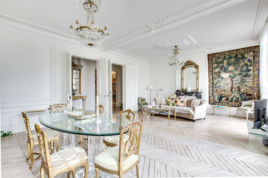 Photo of a large traditional dining room in Paris with white walls, painted wood flooring, a standard fireplace, a stone fireplace surround, white floors and feature lighting.