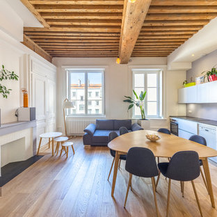 Exemple d'une salle à manger ouverte sur le salon scandinave de taille moyenne avec un mur blanc, un sol en contreplaqué, une cheminée standard, un manteau de cheminée en pierre et un sol beige.