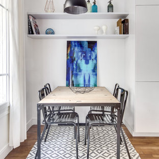 Cette image montre une salle à manger ouverte sur la cuisine traditionnelle avec un mur blanc et un sol en bois brun.
