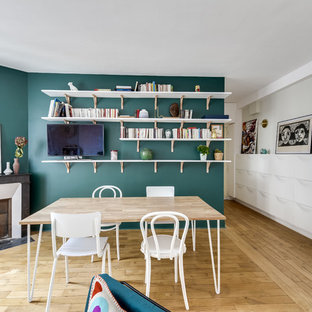 Aménagement d'une salle à manger ouverte sur le salon contemporaine avec un mur vert, un sol en bois clair, une cheminée d'angle et un sol beige.