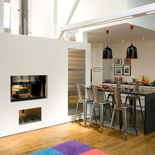 Inspiration pour une salle à manger ouverte sur le salon urbaine avec un mur blanc, un sol en bois brun et une cheminée double-face.