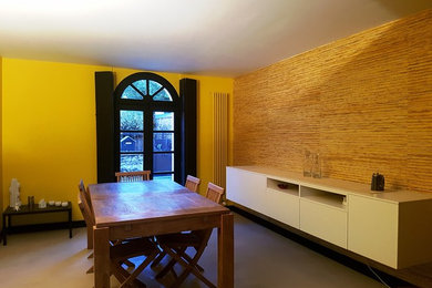 Modelo de comedor actual de tamaño medio abierto con paredes amarillas, suelo de cemento y suelo gris