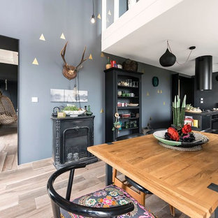 Idée de décoration pour une salle à manger ouverte sur la cuisine bohème de taille moyenne avec un mur gris, un sol en bois clair et une cheminée standard.