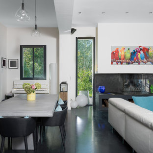 Aménagement d'une salle à manger ouverte sur le salon contemporaine avec un mur blanc, une cheminée ribbon et un sol noir.