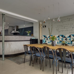 Aménagement d'une salle à manger ouverte sur la cuisine industrielle avec un mur gris, béton au sol et un sol gris.
