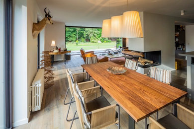 Exemple d'une grande salle à manger ouverte sur le salon tendance avec un mur blanc, un sol en bois brun et une cheminée double-face.