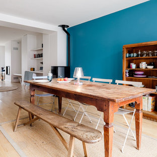 Cette photo montre une salle à manger ouverte sur le salon éclectique avec un sol en bois clair, un mur bleu et un poêle à bois.