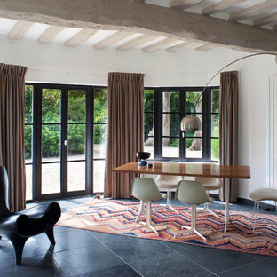 Réalisation d'une salle à manger design avec un mur blanc, un sol en ardoise, un sol noir et un plafond en poutres apparentes.