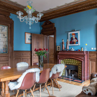 Cette image montre une salle à manger bohème fermée avec un mur bleu, un sol en bois clair, une cheminée standard et un manteau de cheminée en carrelage.