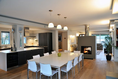 Exemple d'une grande salle à manger ouverte sur le salon tendance avec un mur gris, parquet clair, une cheminée double-face, un manteau de cheminée en béton et un sol beige.