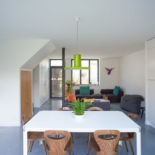 Cette photo montre une salle à manger ouverte sur le salon tendance de taille moyenne avec un mur blanc, béton au sol et aucune cheminée.