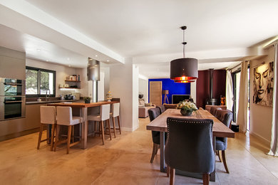 Idée de décoration pour une grande salle à manger ouverte sur la cuisine design avec un mur blanc, un sol en travertin, un poêle à bois, un manteau de cheminée en métal et un sol beige.
