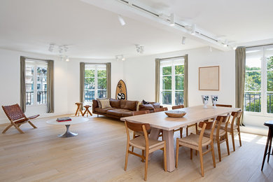 Cette image montre une grande salle à manger ouverte sur la cuisine design avec un mur blanc, parquet clair et un sol beige.
