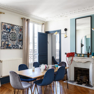 Exemple d'une salle à manger tendance fermée avec un mur blanc, un sol en bois brun, une cheminée standard, un manteau de cheminée en brique et un sol marron.