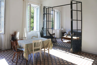 Exemple d'une grande salle à manger ouverte sur le salon méditerranéenne avec un mur blanc, tomettes au sol, une cheminée standard et un manteau de cheminée en pierre.