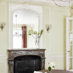 Exemple d'une salle à manger chic fermée et de taille moyenne avec un sol en bois brun, une cheminée standard, un mur jaune et un manteau de cheminée en pierre.