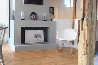 Cette image montre une petite salle à manger ouverte sur le salon urbaine avec un mur blanc, parquet clair, une cheminée standard et un manteau de cheminée en plâtre.