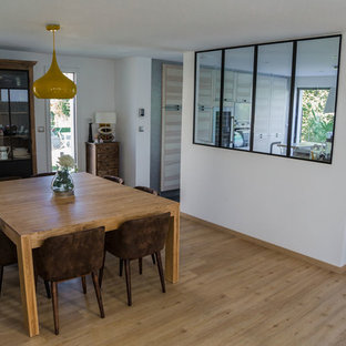 Cette photo montre une grand salle à manger ouverte sur la cuisine industrielle avec un mur blanc, un sol en bois clair et un sol beige.