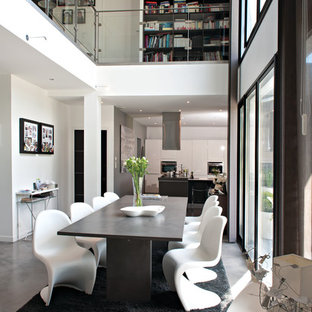 Cette photo montre une salle à manger ouverte sur le salon tendance avec un mur blanc et béton au sol.
