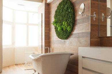 Cette photo montre une salle de bain principale tendance de taille moyenne avec des portes de placard blanches, une baignoire sur pieds et un sol en bois brun.