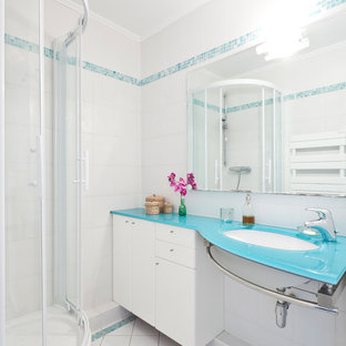 Idée de décoration pour une salle d'eau design de taille moyenne avec un lavabo encastré, un placard à porte plane, un plan de toilette en verre, une douche d'angle, un carrelage blanc, un mur blanc, un sol en carrelage de porcelaine, des portes de placard blanches et un plan de toilette bleu.